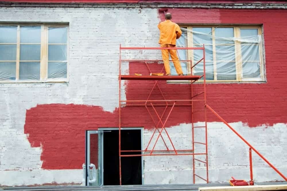 trabajador pintando de rojo fachada edificio